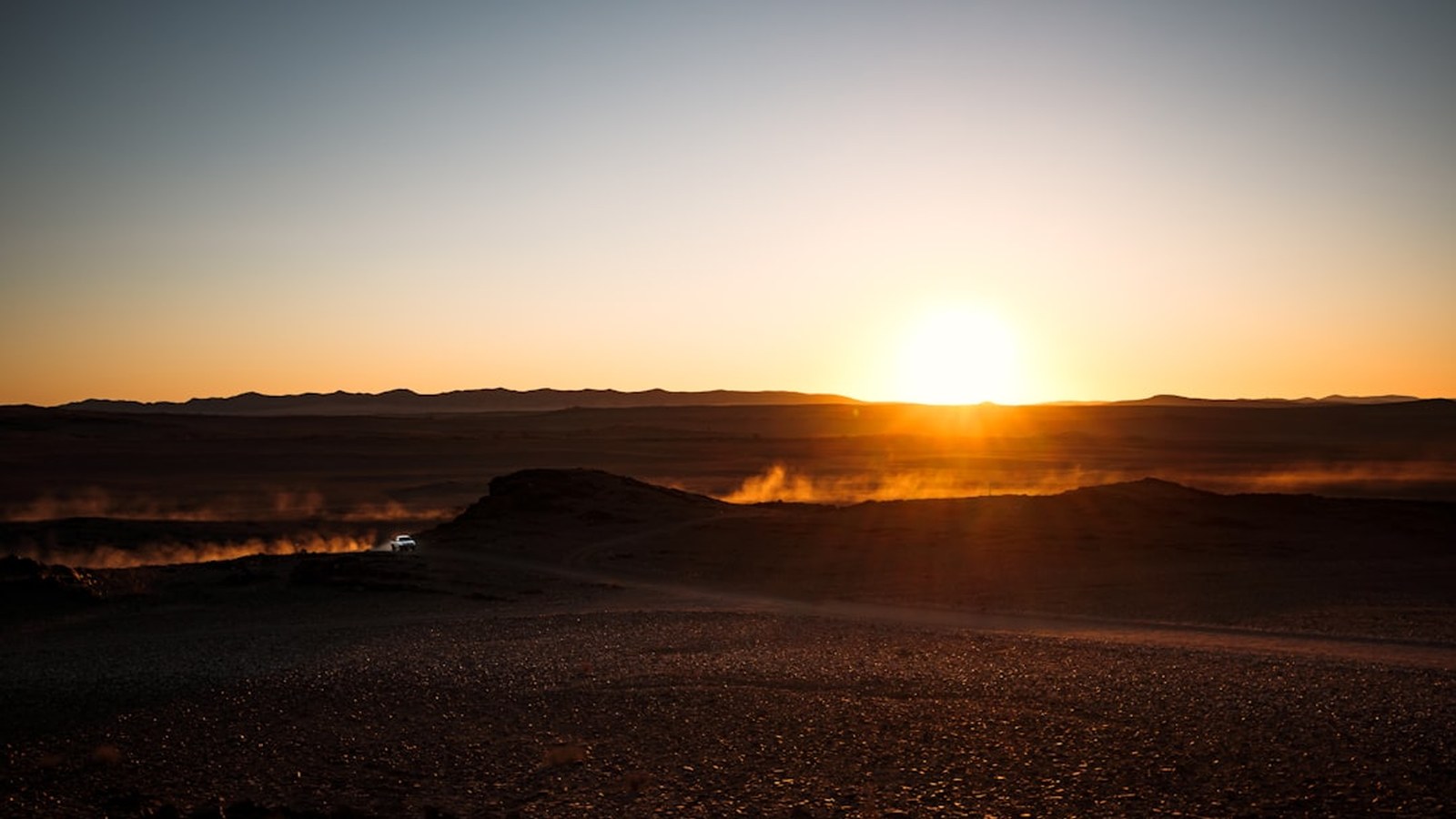A single overland rig kicks up dust in a vast, empty desert at sunset, far from any cell coverage.