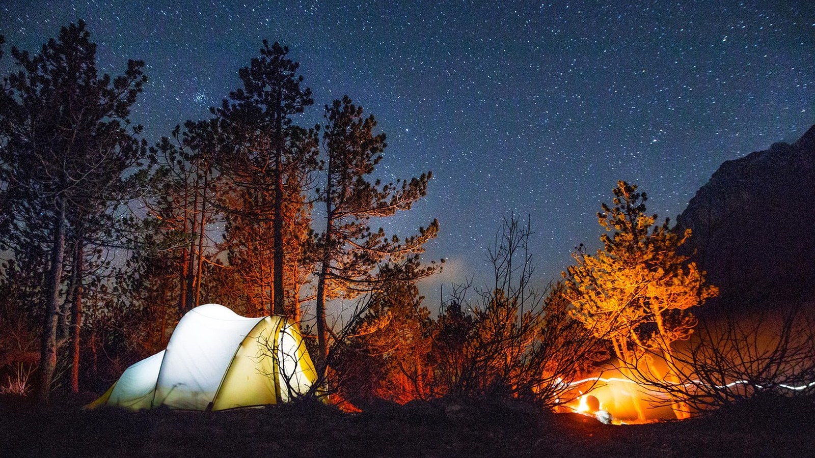 A glowing tent under a sky full of stars at a remote backcountry family camp.