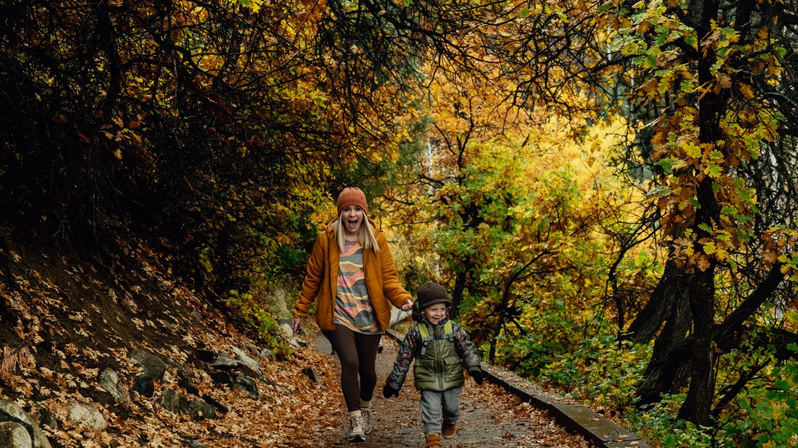 A parent and child hiking a golden autumn forest trail on a family overland trip.