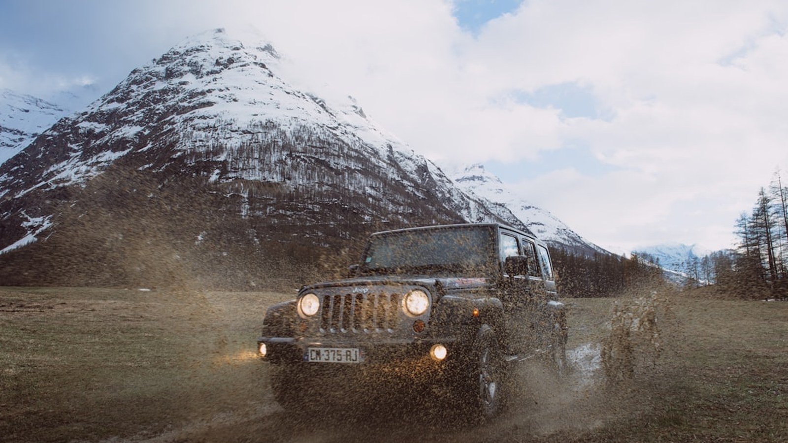 A Jeep Wrangler throwing a spray of trail mud and water on a mountain trail after a hard off-road run
