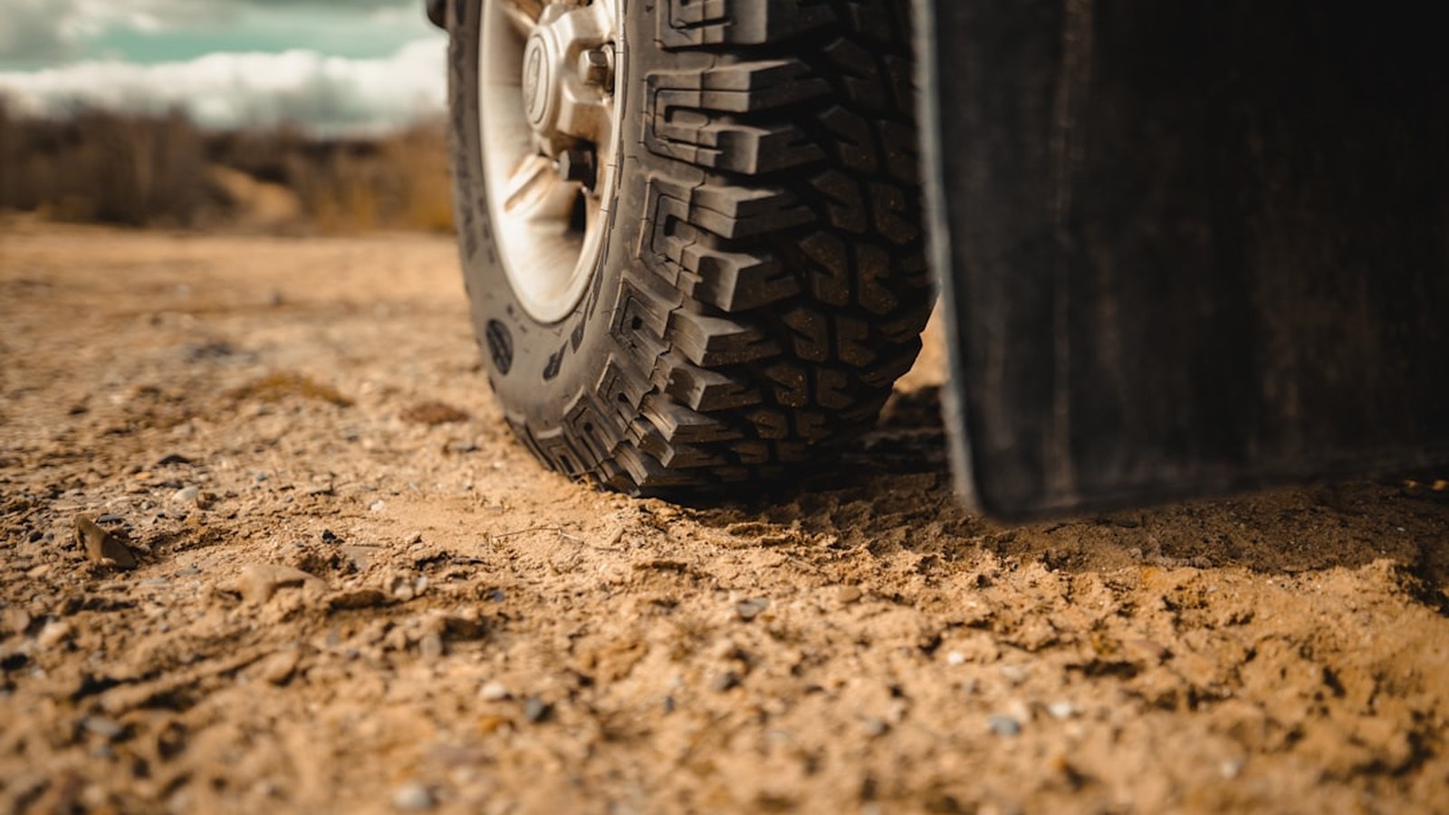 Aggressive off-road mud-terrain tire and alloy wheel photographed low and close, showing deep tread lugs