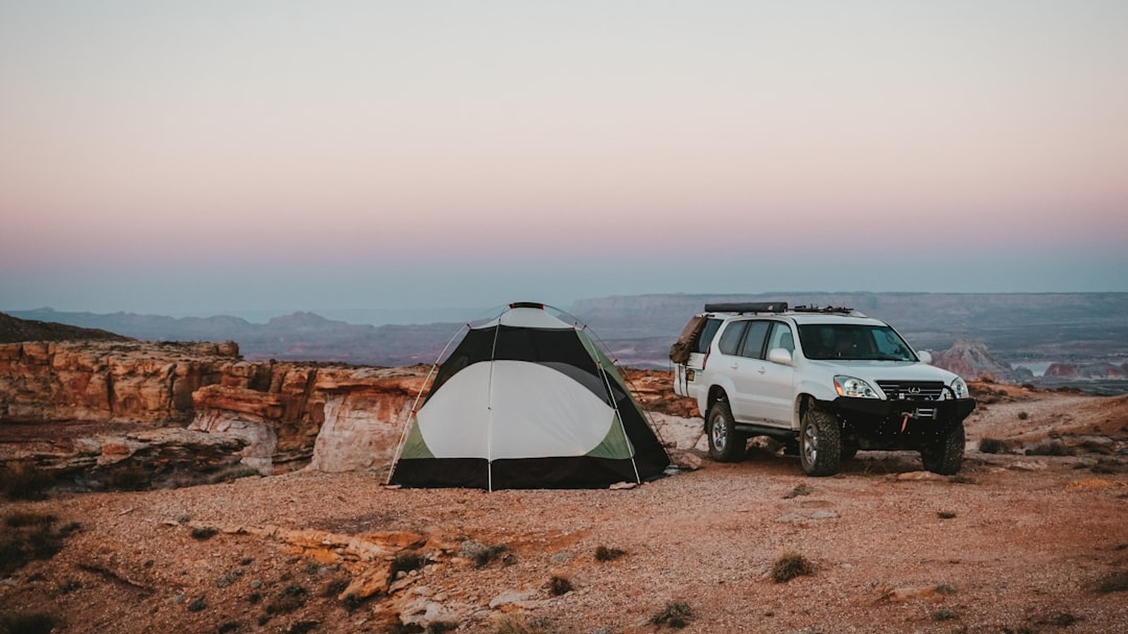 An overland 4x4 rig with a rooftop tent camped at a desert canyon rim at dusk