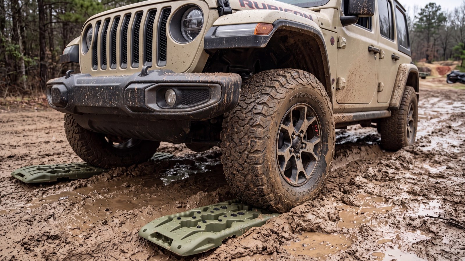 Green recovery traction boards wedged under the tire of a Jeep Wrangler Rubicon in mud