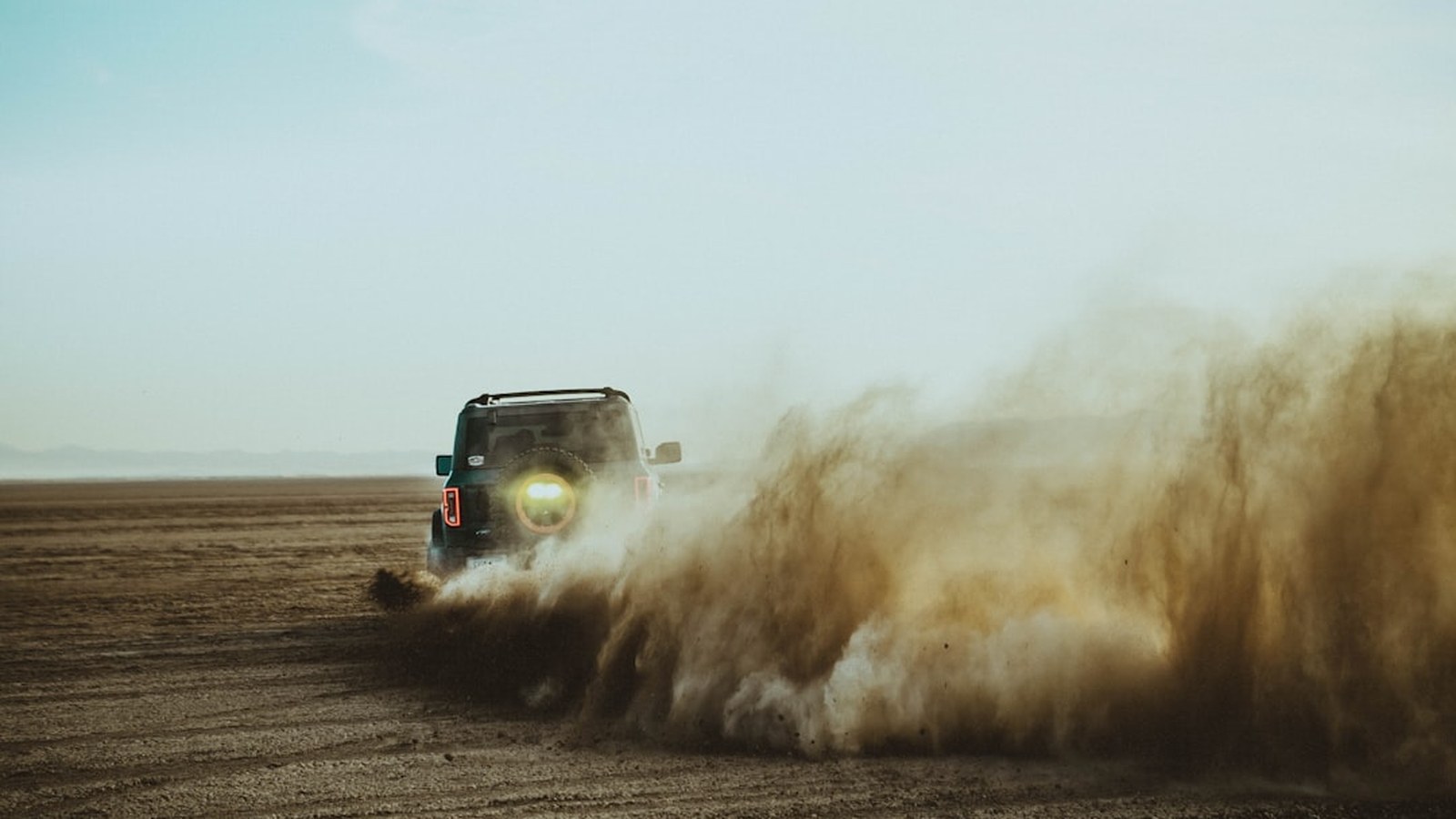 4x4 truck throwing a large dust plume while driving a desert trail
