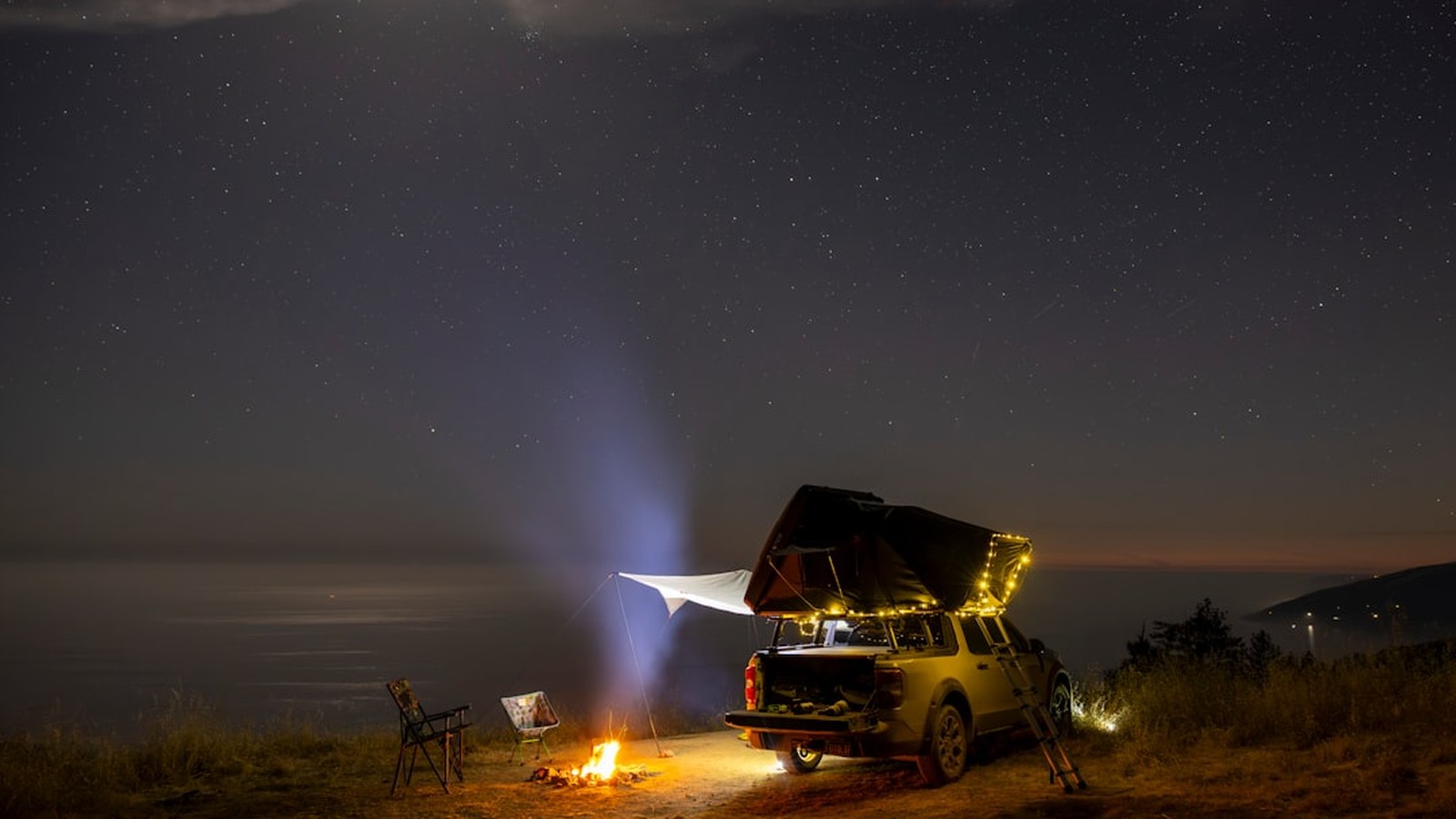 Land Rover Defender with a rooftop tent open at a mountain sunset camp