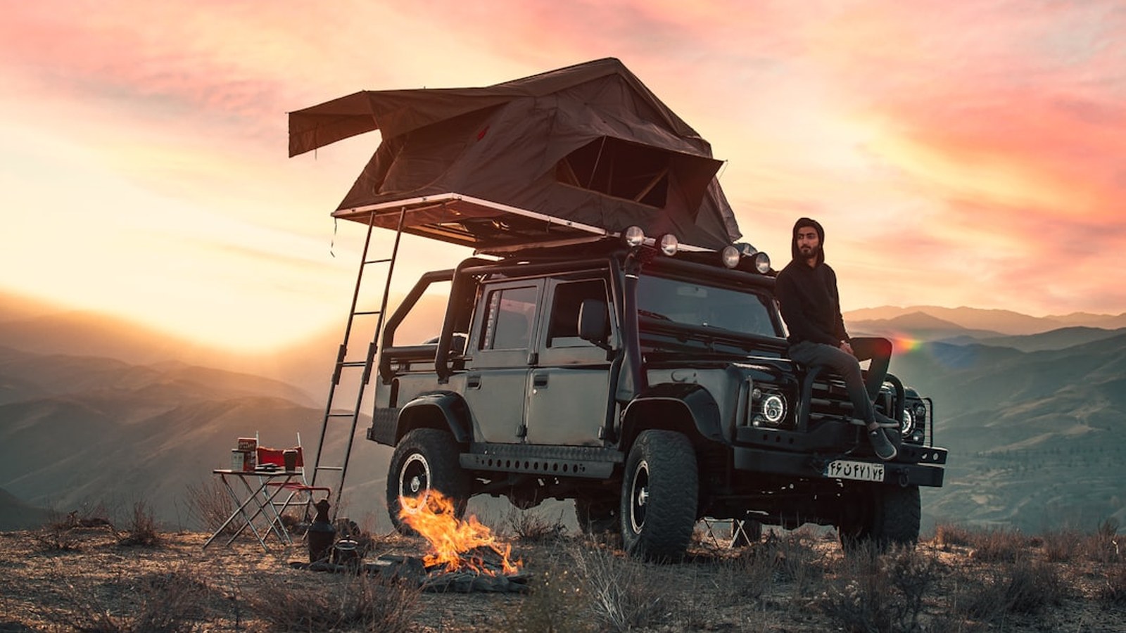 White pickup with a hardshell rooftop tent open on a coastal bluff at sunset