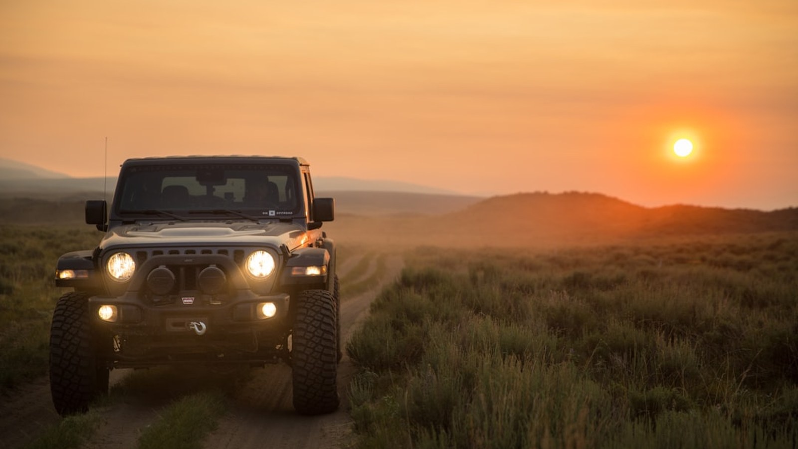 Jeep driving a trail into a golden-hour sunset