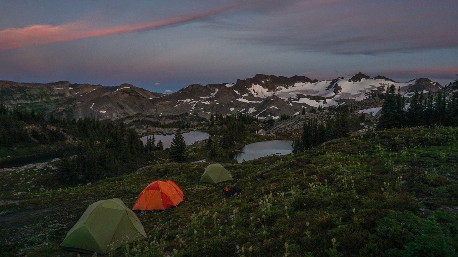 Tents at a mountain campsite glowing at sunset with peaks in the distance