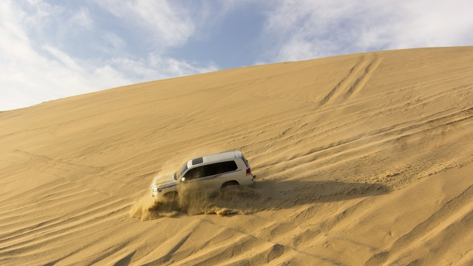 A 4x4 descending a steep dune with a plume of sand, tires aired down for the soft terrain