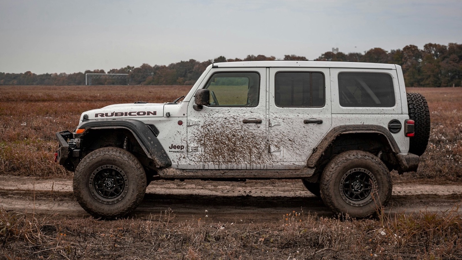 A mud-splattered Jeep Wrangler on a dirt trail after a run