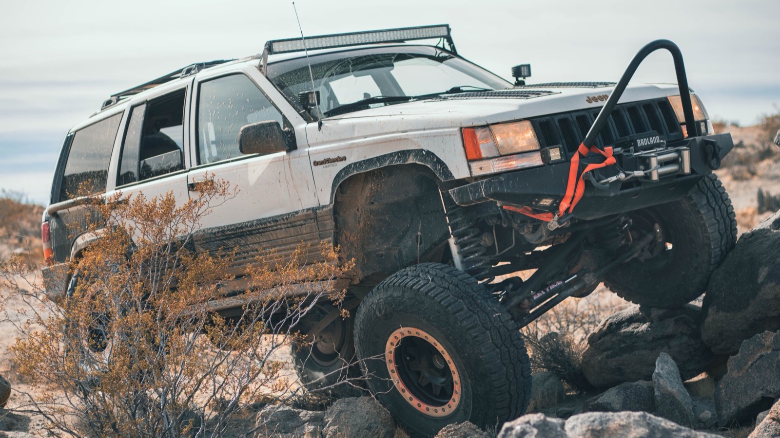A built 4x4 with a winch and big tires flexing over rocky terrain