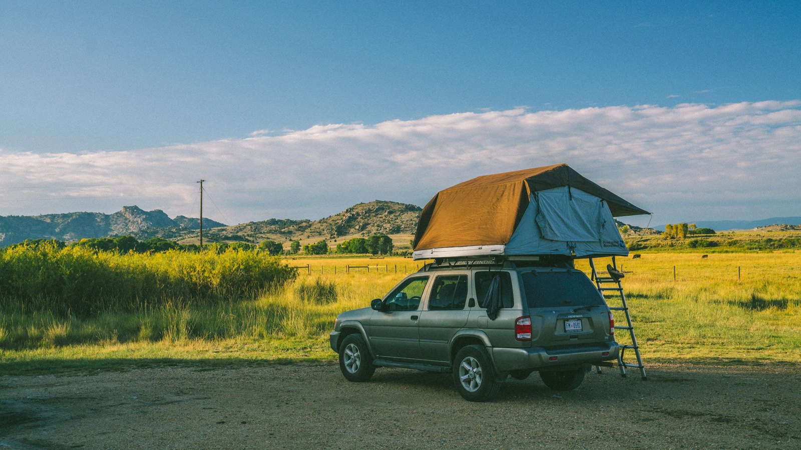 An SUV with a deployed rooftop tent in a scenic golden grassland