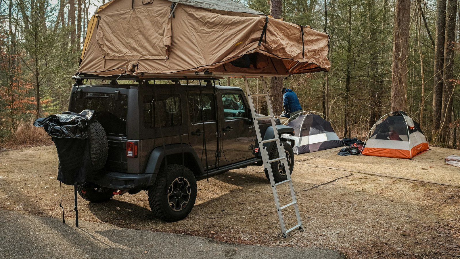 An open rooftop tent with its ladder deployed at a wooded campsite