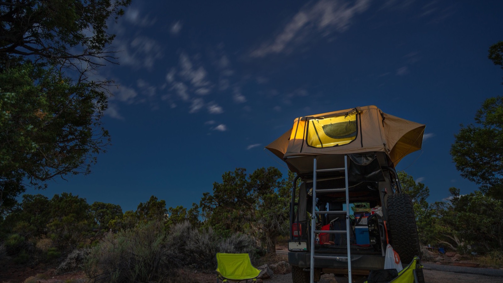 A rooftop tent glowing on a rig under a starry desert sky