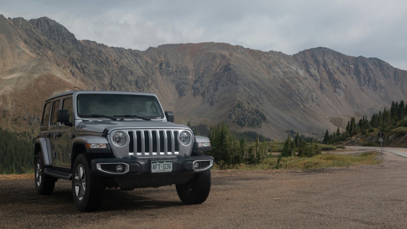 A Jeep Wrangler parked at a high alpine pass with sweeping San Juan range views above Ouray