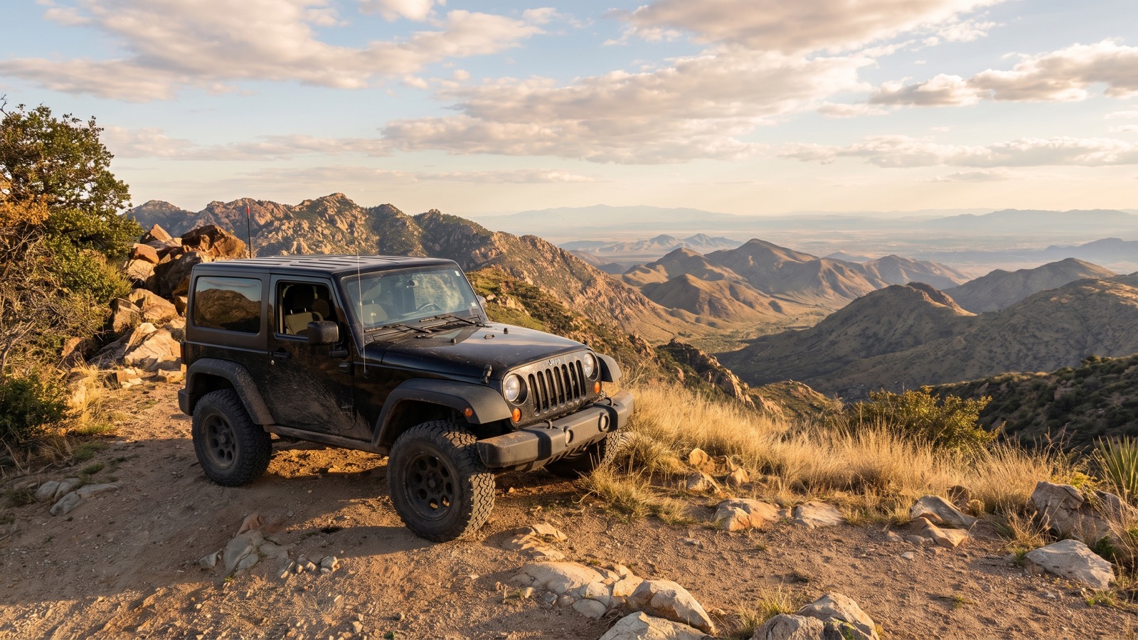 A black Jeep Wrangler parked at a ridge overlook at golden hour, layered desert mountains fading into the distance.