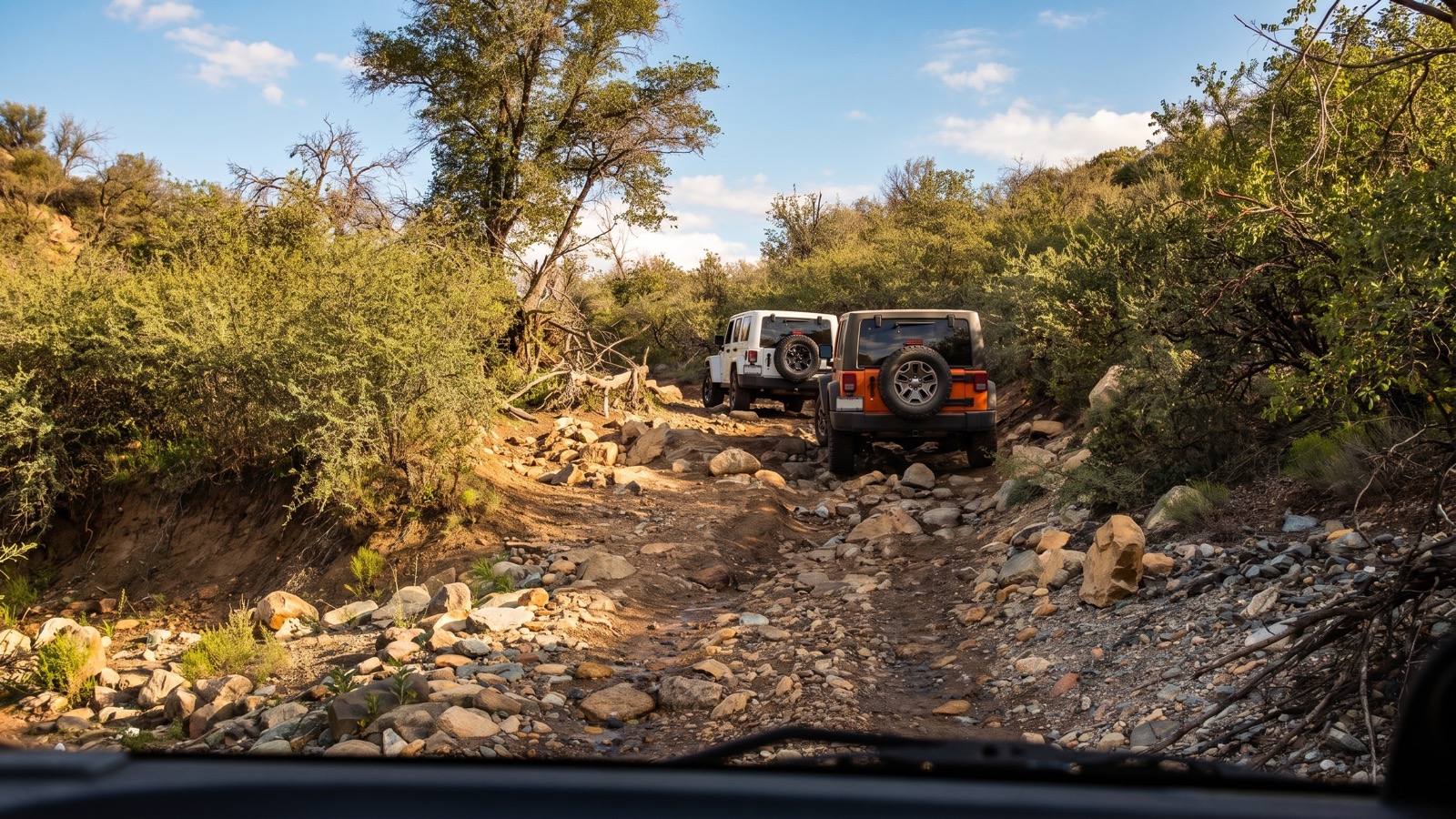 Two Jeeps working down a rocky, boulder-strewn creek wash on the trail, seen from the driver's seat.