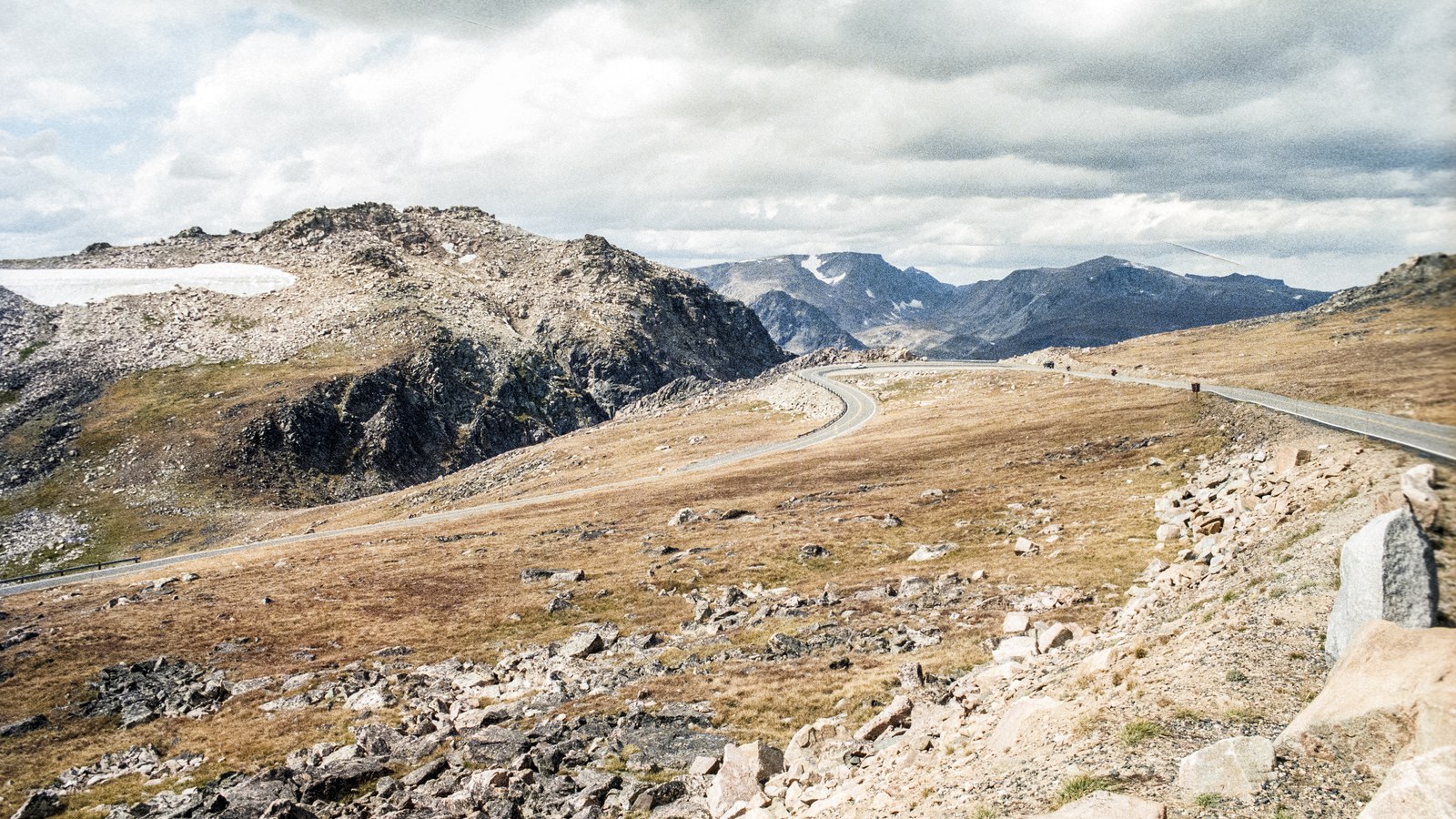 The Beartooth Highway crossing the barren high alpine plateau with snowfields and distant rocky peaks under a moody sky