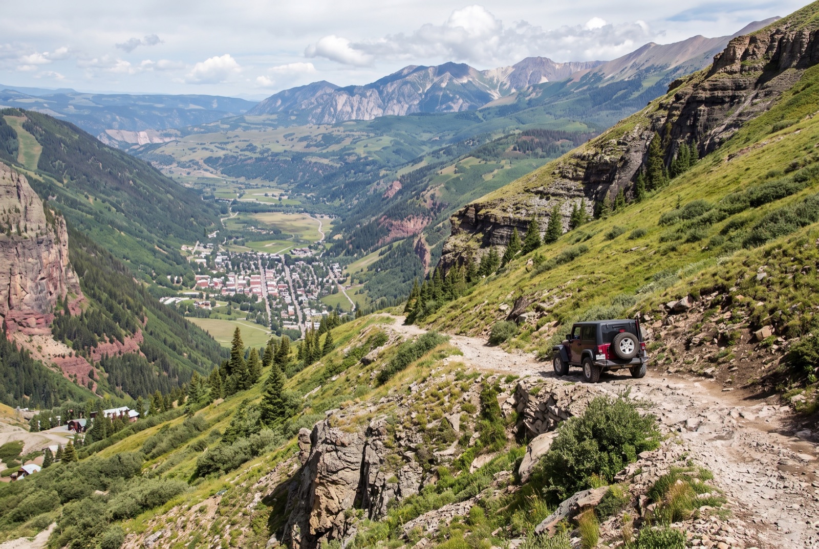 The narrow shelf road of Black Bear Pass descending toward the green Telluride valley floor below the San Juan peaks