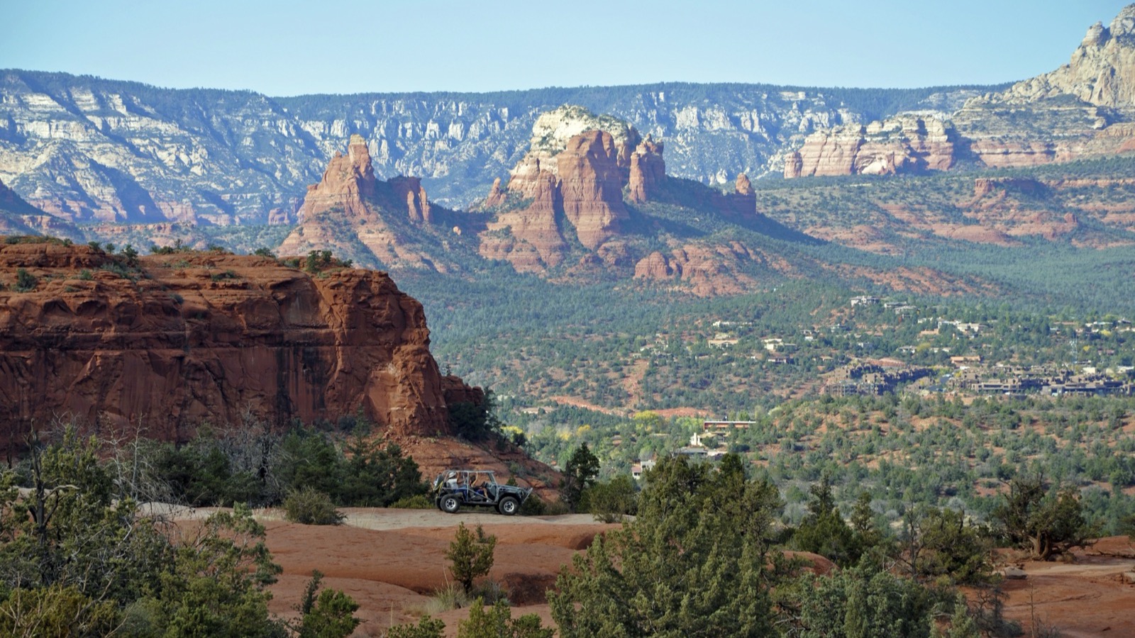 A 4x4 parked on red slickrock above the Sedona valley along Broken Arrow, with red-rock spires in the background