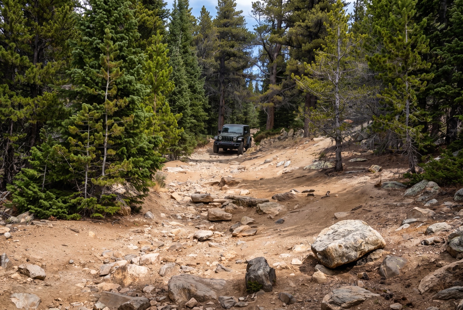 A high-clearance 4x4 easing up the rough dirt forest road that climbs toward Chinns Lake, gentle rounded high-country ridges in the distance