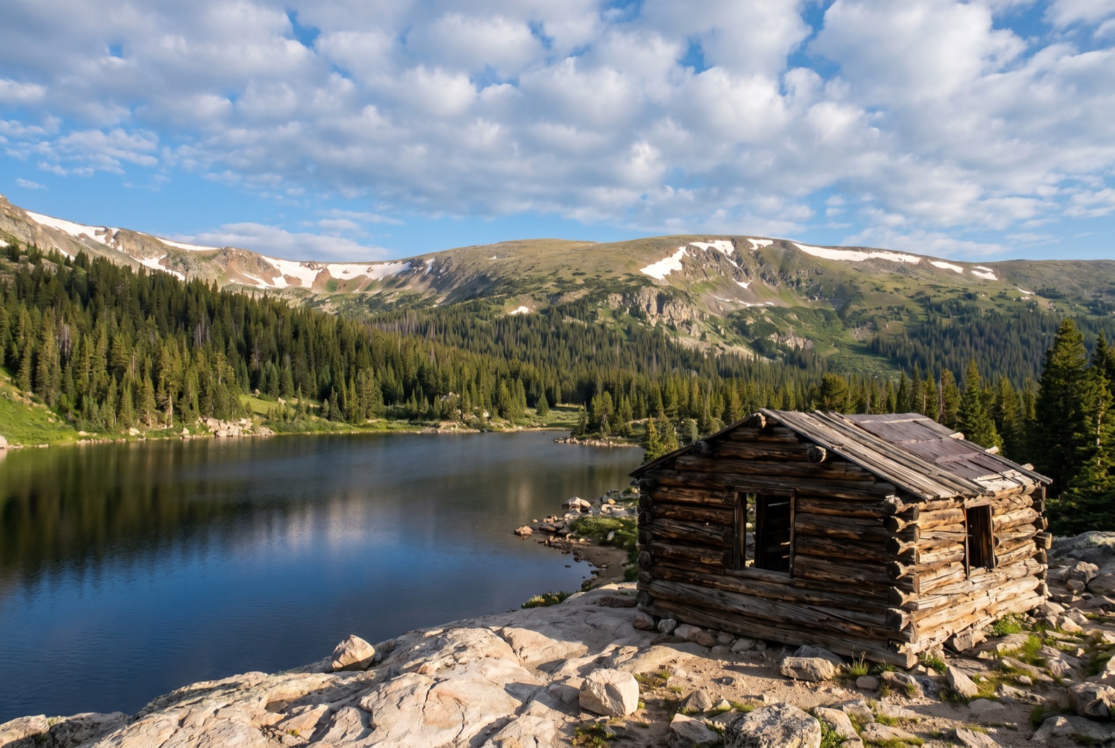 A calm alpine lake at Chinns Lake ringed by spruce and pine with gentle rounded timberline ridges reflected in the still water