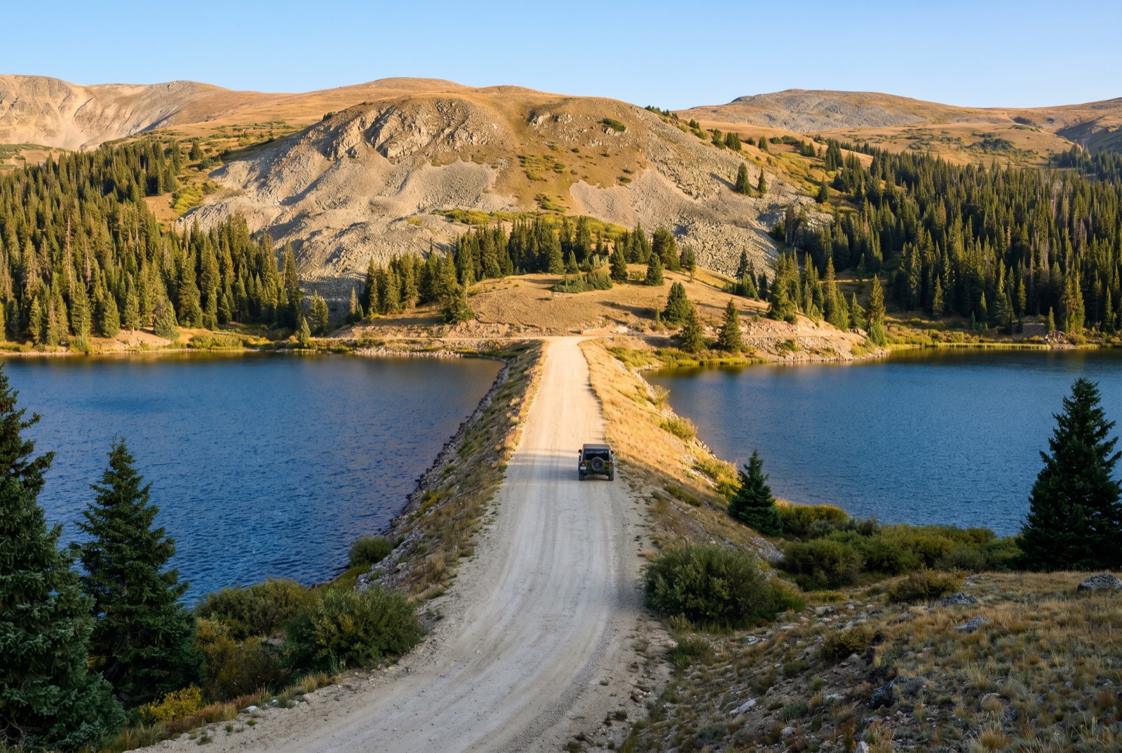 Aerial view of the two Chinns reservoirs sitting side by side in a narrow timberline basin, with the dirt Chinns Lake road threading right between the two lakes