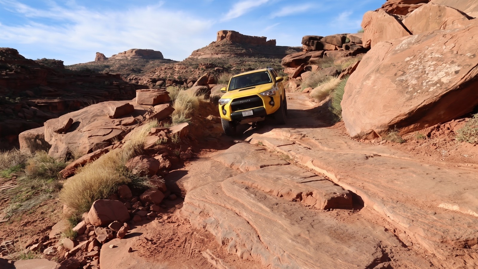 A red Jeep Wrangler crawls the narrow sandstone shelf of the Cliffhanger obstacle above Jackson Hole canyon, Moab Utah