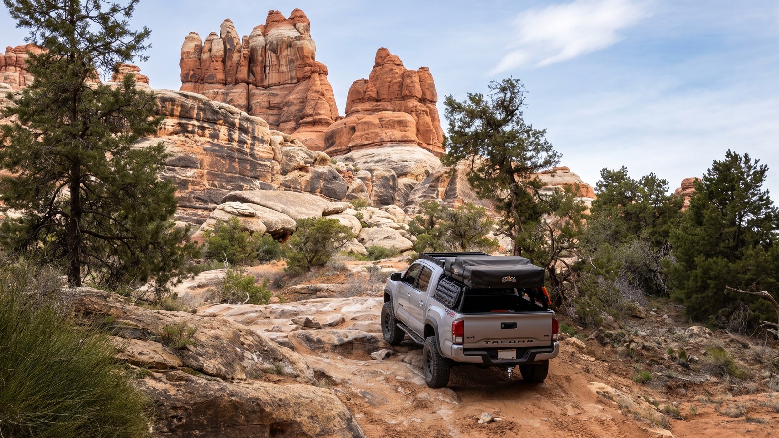 A Toyota Tacoma with a rooftop tent parked below the banded sandstone spires of the Needles District along the Elephant Hill trail.