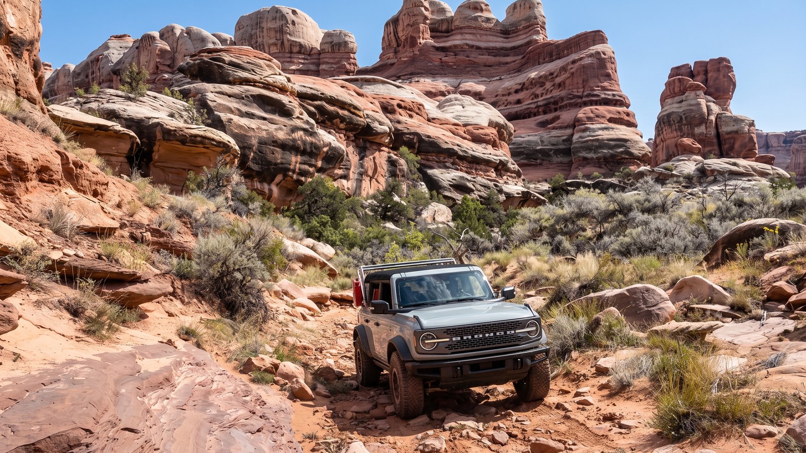 A rugged Ford Bronco working up a rocky red gully below the banded Cedar Mesa sandstone cliffs of the Needles District on the Elephant Hill trail.