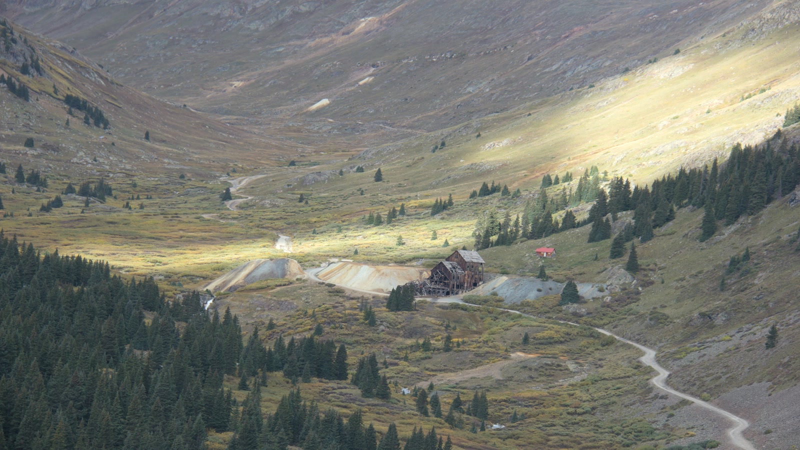 The old mill at Animas Forks lit by a shaft of light, autumn color filling the high mining valley