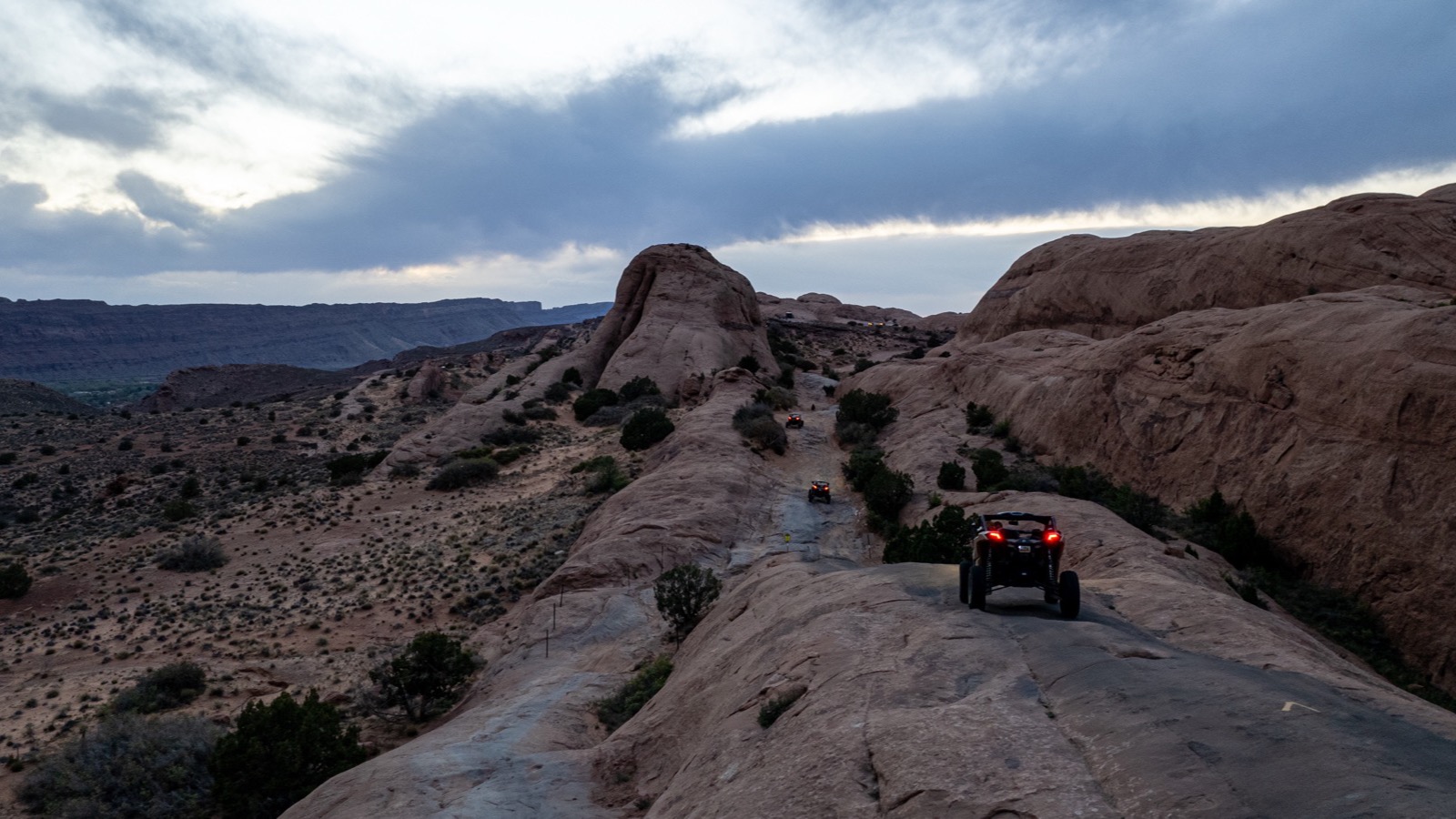 Side-by-sides descending a slickrock fin on a Moab 4x4 trail at dusk
