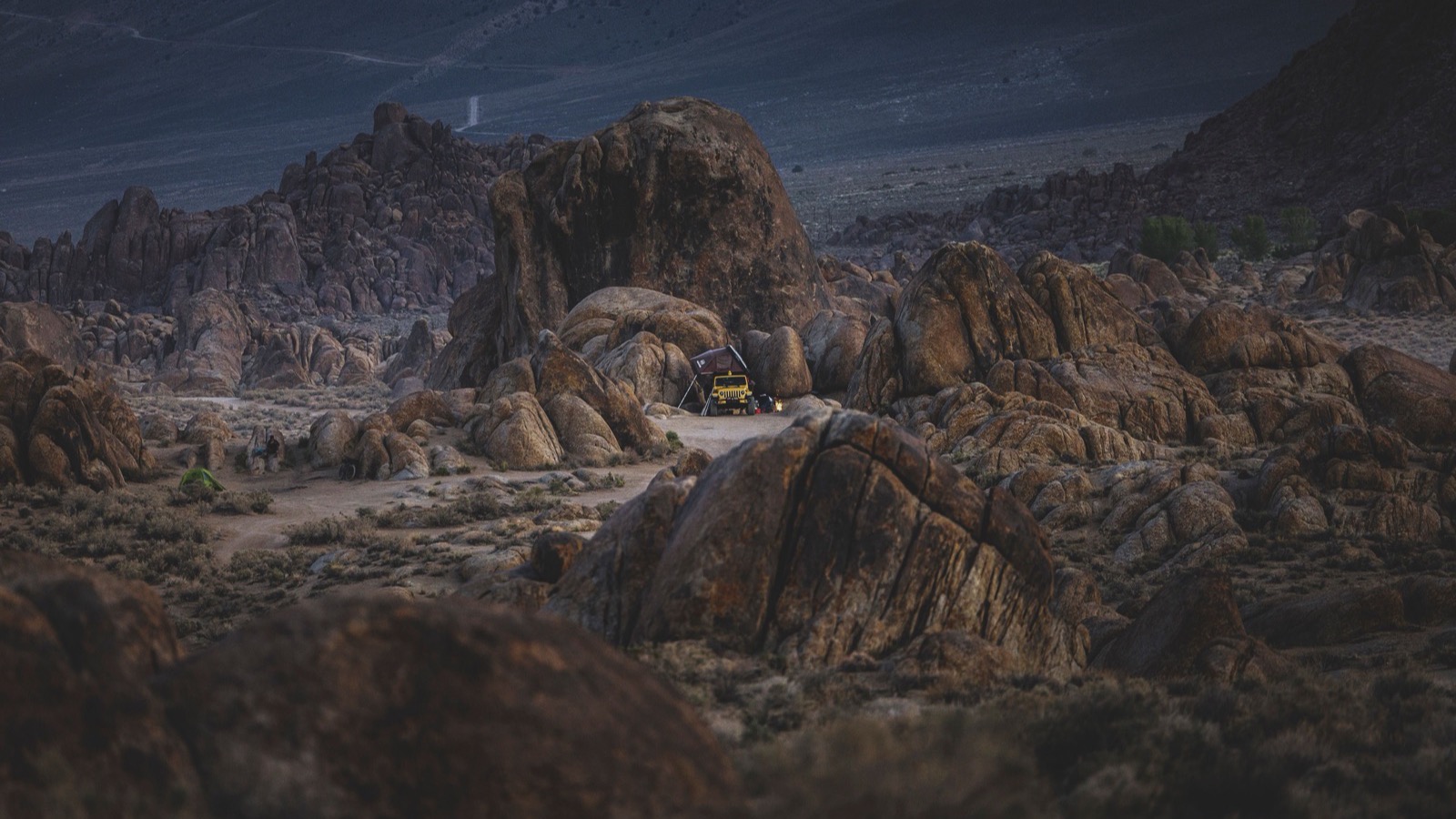 A Jeep Wrangler with a rooftop tent set up among red rock boulders near Moab at dusk