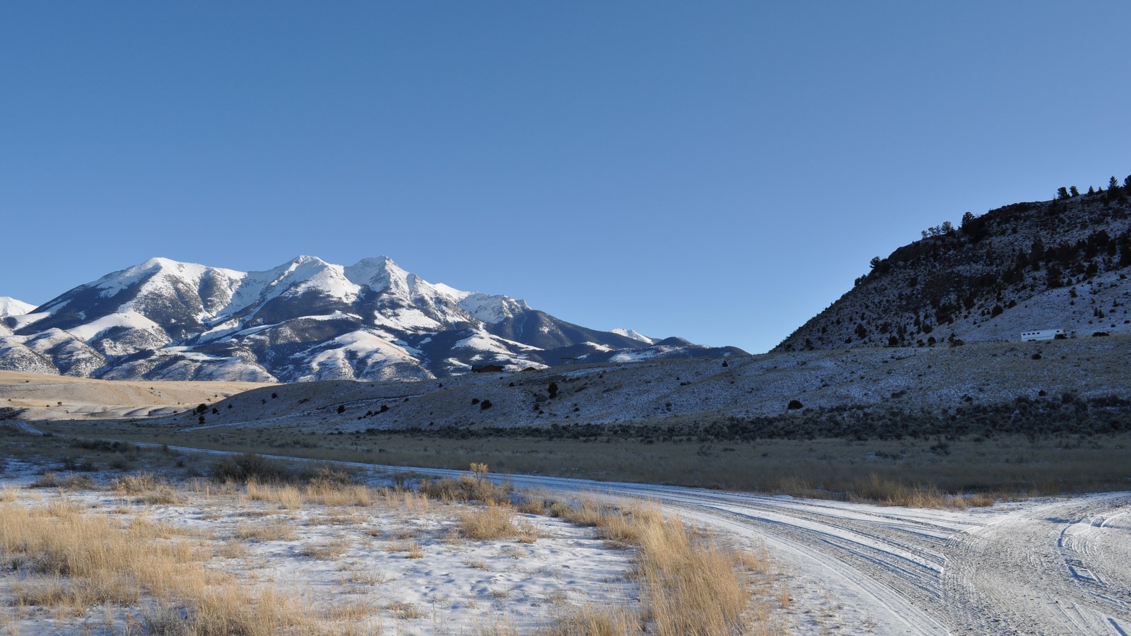 Dirt road curving through sagebrush toward the snow-dusted Absaroka Range near Gardiner, Montana