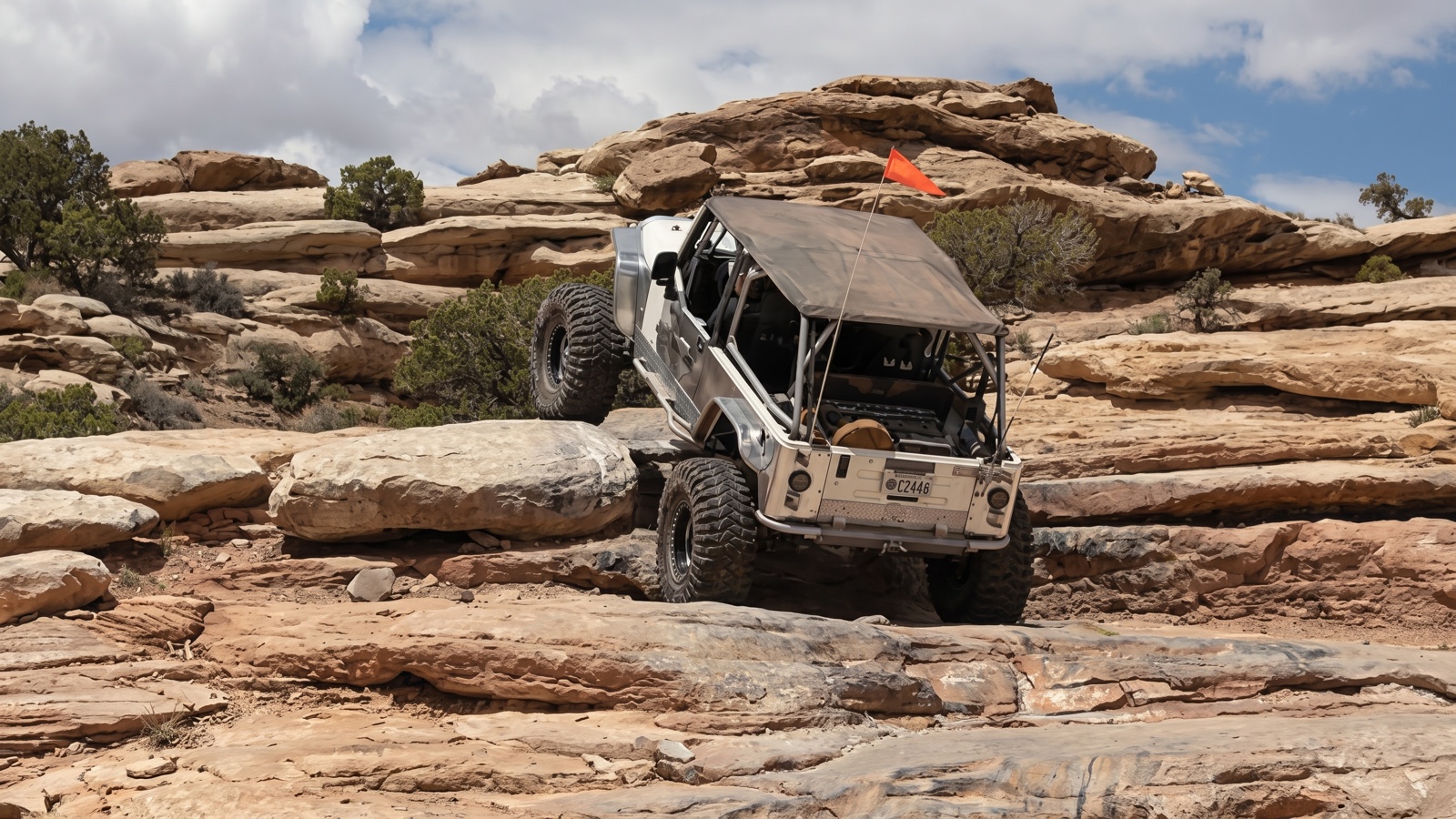 A tube-chassis rock buggy climbing stacked sandstone ledges among juniper on Golden Spike Trail in Moab