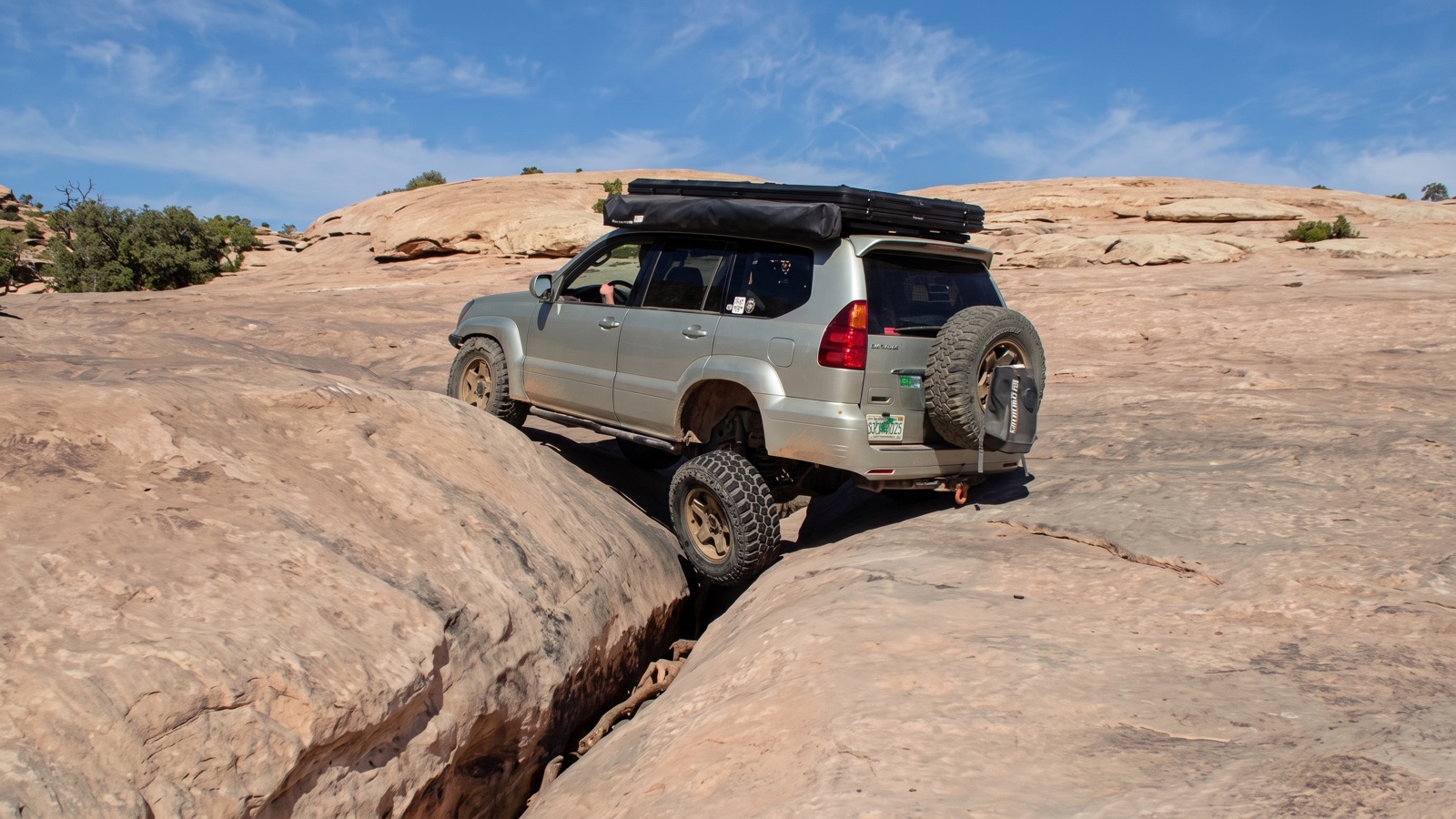 A modified 4x4 SUV with a rear tire carrier bridging the narrow Golden Crack slot in the Moab slickrock