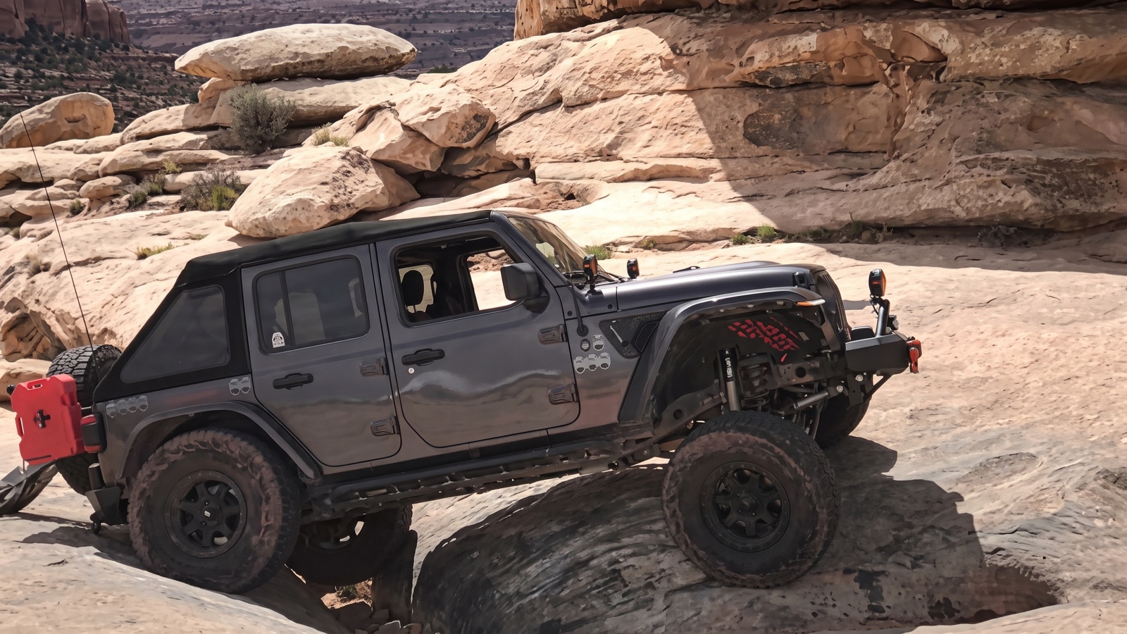 A dark gray Jeep Wrangler cresting the top of a steep slickrock ledge obstacle on Golden Spike Trail in Moab