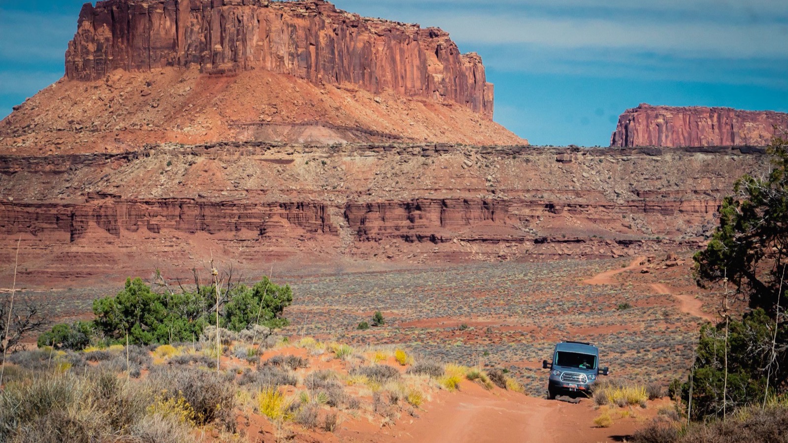 An overland rig on a red rock two-track below a massive Moab butte near the Sand Flats Recreation Area