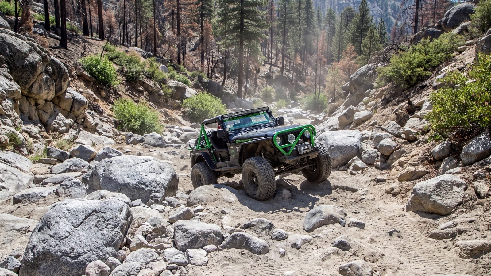 A caged 4x4 being winched and spotted up a tough boulder section on Holcomb Creek.