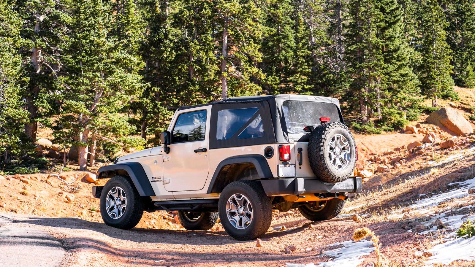A Jeep Wrangler navigating a rocky alpine Colorado forest road on the approach to a high-altitude 4x4 trail, Sawatch Range spruce forest all around