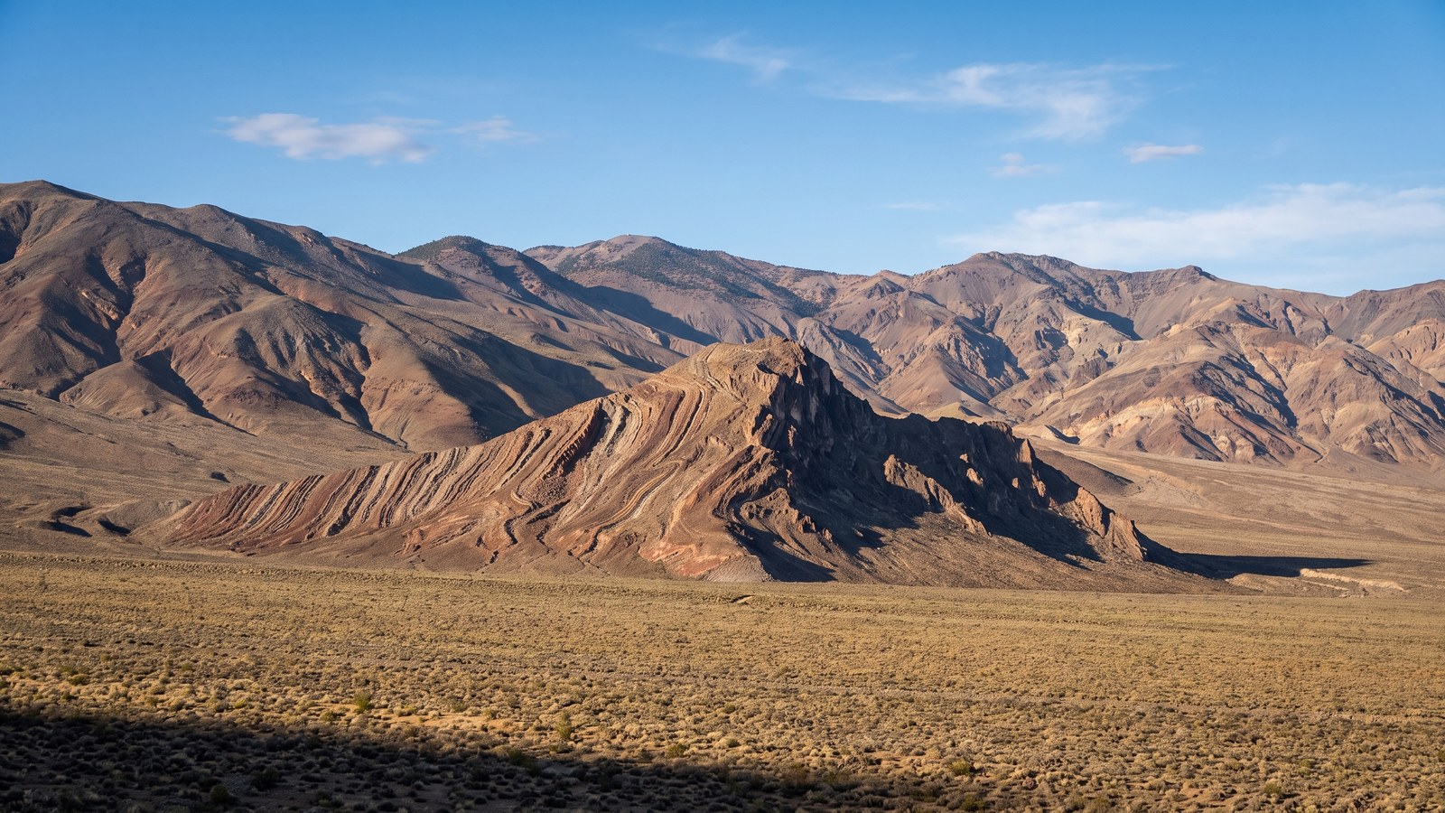 A wide high-desert valley in the Panamint Range framed by mountains, with the distinctive tilted, banded rock of Striped Butte rising from the valley floor