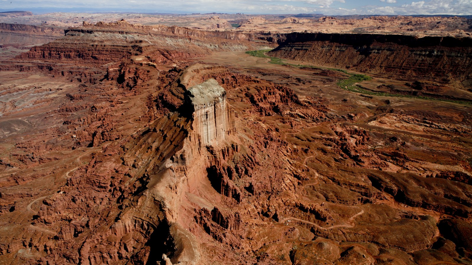 A tall layered sandstone butte rising above the eroded Moab canyon country, with a faint 4x4 track threading the bench below