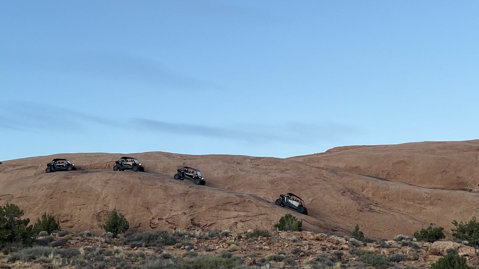 Side-by-sides working their way across the bare red slickrock of the Moab area, the same tilted Kayenta and Navajo sandstone the Rim Trail climbs