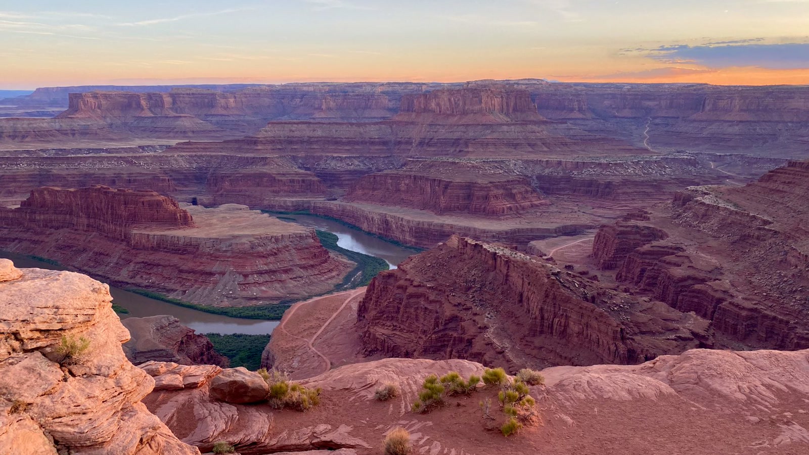 The Colorado River winding far below towering red sandstone cliffs in the Moab canyon country, the kind of view that opens up from the mesa rim