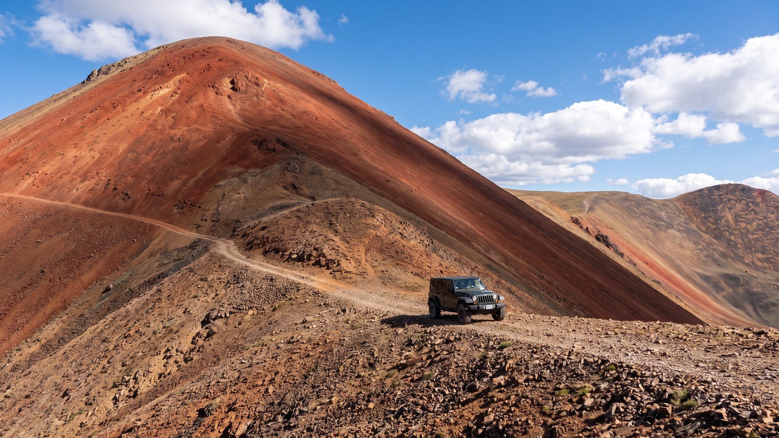 A 4x4 on the shelf road beside the striking reddish cinder cone of Red Cone Peak, high above treeline