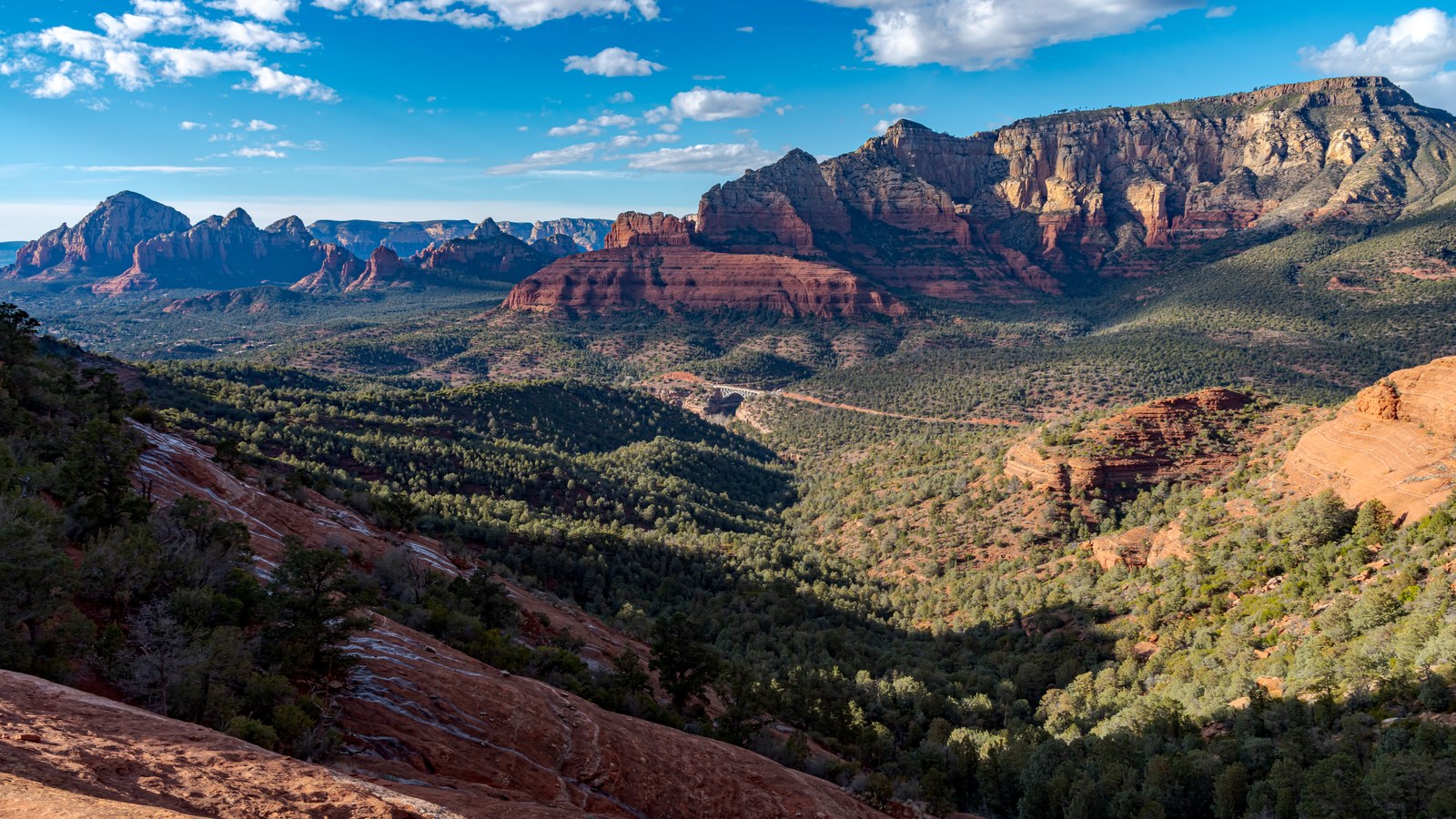 A sweeping overview from the Mitten Ridge slickrock above Schnebly Hill Road, looking out over the green valley and red rock ridgelines toward Sedona