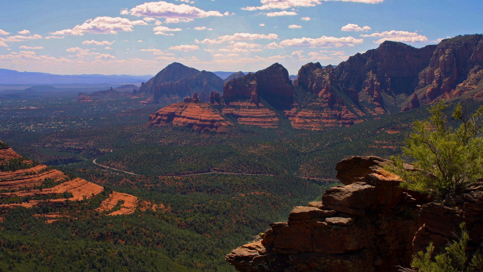 Layered red rock peaks of the Mitten Ridge area towering above the green valley along Schnebly Hill Road near Sedona, Arizona