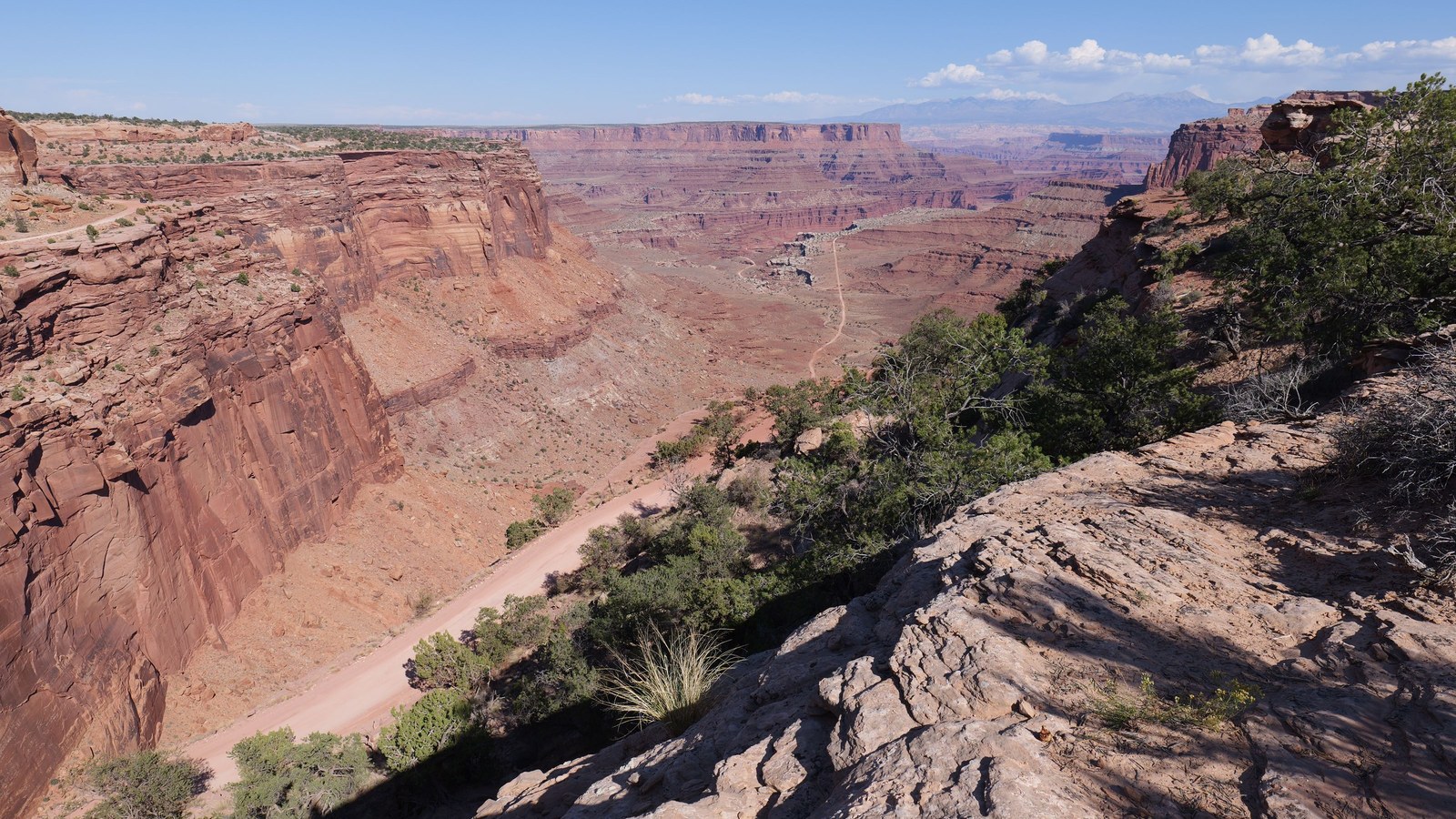 A red-rock canyon near Moab with a graded dirt road winding below the rim, the kind of easy approach two-track that leads toward Waring Mesa