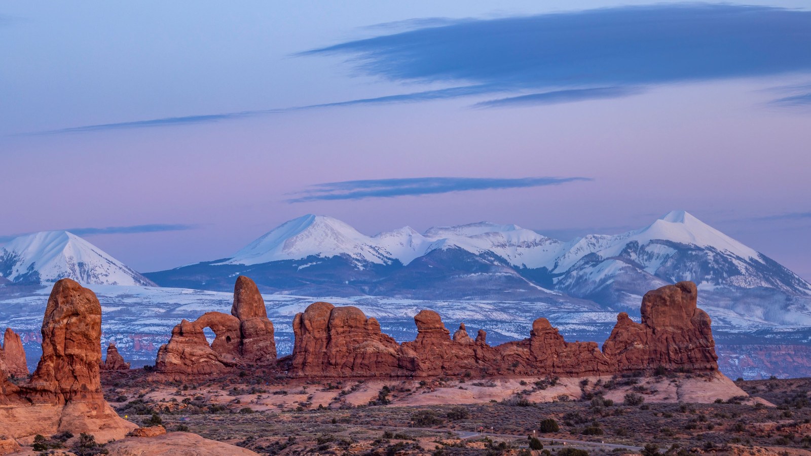 Snowcapped La Sal Mountains rising behind glowing red-rock formations near Moab at dusk