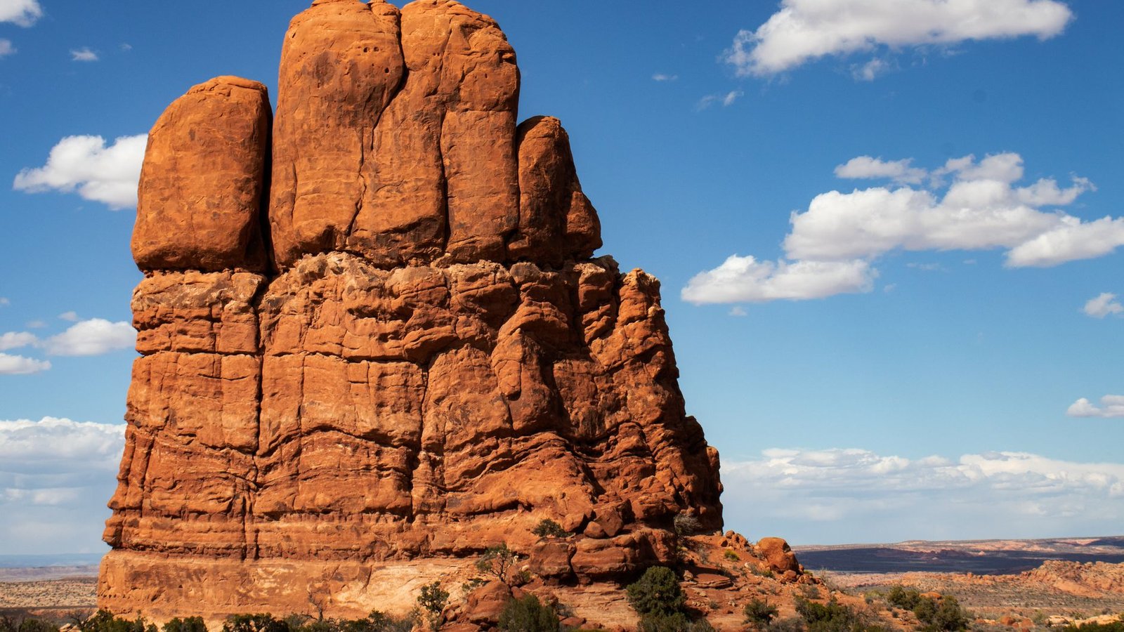 A bold isolated red sandstone monolith rising under a deep blue sky in the Moab high desert, the kind of landmark the trail passes on its way up
